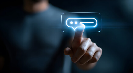 A man's fingertip presses a glowing blue chat bubble icon in mid-air, signifying communication, online interaction, and digital connectivity. The image evokes a sense of interaction, communication.