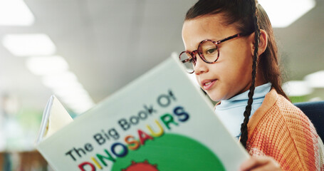 Girl, child and education with reading book at library with literacy, learning and glasses for...
