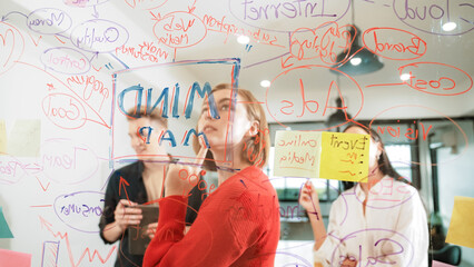 Creative business team brainstorming and sharing marketing idea about start up project by writing down on colorful sticky note at glass board modern meeting room. Working together. Immaculate.