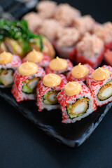 Assorted sushi rolls with fish, shrimp, and seafood served on a black plate. Gourmet Japanese cuisine with colorful ingredients. Overhead view, minimal background.