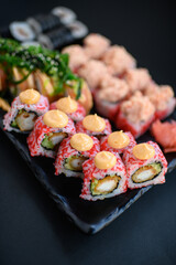 Assorted sushi rolls with fish, shrimp, and seafood served on a black plate. Gourmet Japanese cuisine with colorful ingredients. Overhead view, minimal background.