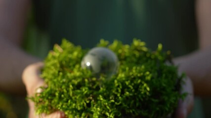 a mini glass globe on green moss in male hands close up, symbolizing environmental awareness, responsibility, and sustainability. earth, nature, environment