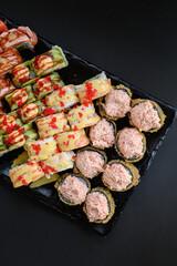 Assorted sushi rolls with fish, shrimp, and seafood served on a black plate. Gourmet Japanese cuisine with colorful ingredients. Overhead view, minimal background.