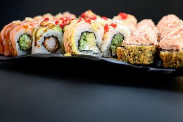 Assorted sushi rolls with fish, shrimp, and seafood served on a black plate. Gourmet Japanese cuisine with colorful ingredients. Overhead view, minimal background.