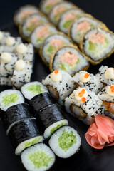Assorted sushi rolls with fish, shrimp, and seafood served on a black plate. Gourmet Japanese cuisine with colorful ingredients. Overhead view, minimal background.