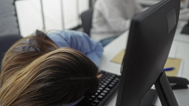 Man awakens woman sleeping at office desk showcasing workplace teamwork and fatigue, with computer and documents visible, in modern indoor business setting.