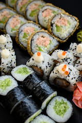 Assorted sushi rolls with fish, shrimp, and seafood served on a black plate. Gourmet Japanese cuisine with colorful ingredients. Overhead view, minimal background.