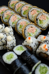 Assorted sushi rolls with fish, shrimp, and seafood served on a black plate. Gourmet Japanese cuisine with colorful ingredients. Overhead view, minimal background.