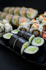 Assorted sushi rolls with fish, shrimp, and seafood served on a black plate. Gourmet Japanese cuisine with colorful ingredients. Overhead view, minimal background.