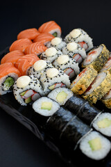 Assorted sushi rolls with fish, shrimp, and seafood served on a black plate. Gourmet Japanese cuisine with colorful ingredients. Overhead view, minimal background.