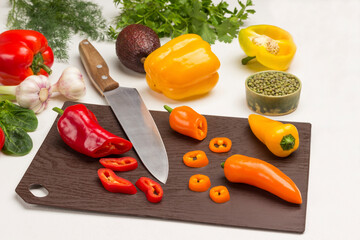 Kitchen knife and slices of chopped pepper on cutting board.