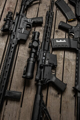 Multiple black tactical rifles and magazines laid out on wooden surface