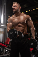 muscular man lifts dumbbells in well equipped gym during evening. He exhibits strong determination...