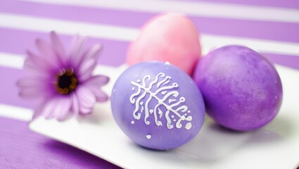 Purple eggs with white writing on them, sitting on a purple cloth.