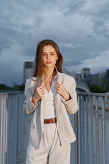 Confident woman in business attire standing outdoors against a dramatic skyline, showcasing modern elegance and professionalism, with a neutral color palette.
