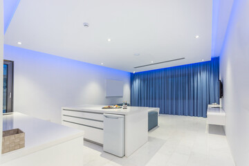 Stylish hotel room with white decor of walls and furniture and blue curtains on the panoramic window.
