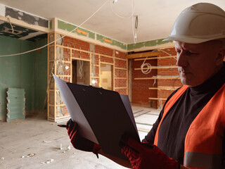 Construction supervisor in safety gear inspects and documents progress inside a partially renovated...