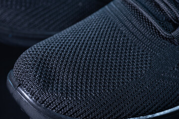 A detailed macro of a black sneaker showing off a textured knit toe, minimalist lacing system, and sleek design. Perfect for a modern sportswear visual.