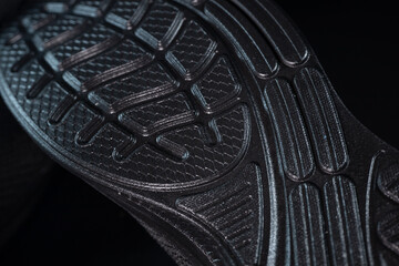 A close-up of a dark rubber shoe sole with curved grooves and a geometric tread design, showcasing...