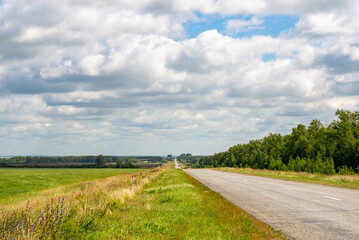 Obraz premium A road and a green field with a sky with clouds