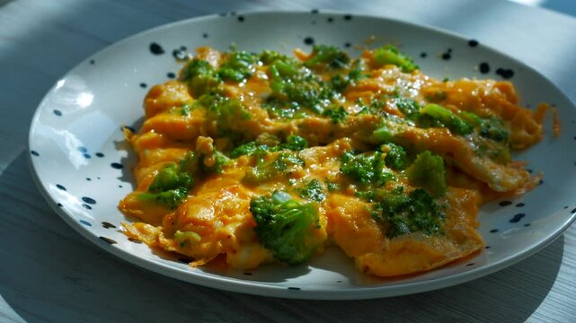 Yellow omelette in a frying pan with vegetables and cheese.
Scrambled eggs with cheese in a hot frying pan close-up.
A person stirs an omelette with a spatula.
Fresh raw eggs