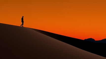 A person walks alone on a dune at sunset