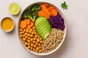 Top view of a colorful vegan buddha bowl with chickpeas, avocado, quinoa, carrots, red cabbage and broccoli, served with dressing and lime.