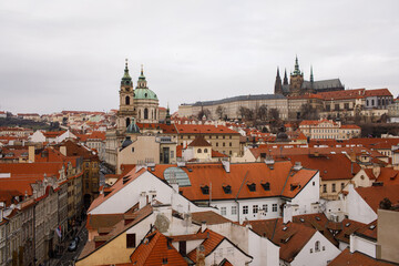 Obraz premium Panoramic view of Prague with red rooftops and historic landmarks, including Prague Castle and St. Vitus Cathedral, showcasing European architecture and cityscape charm
