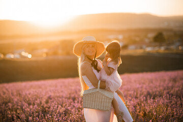 Young woman with child girl 2-3 year old holding straw basket wearing hat in lavender field...