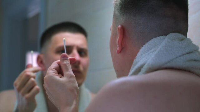 A man cleans his ears in front of a mirror.
Body care.
Cotton swab and man in front of a mirror.
A man is washing and cleaning his ears.
Ears, ear health, hygiene and cleanliness
