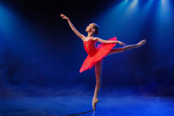 Little Ballerina gracefully dances in pointe shoes on stage in bright red tutu against dramatic spotlight background