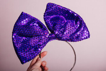 Sparkly purple bow headband held in hand, perfect for party or costume accessories.