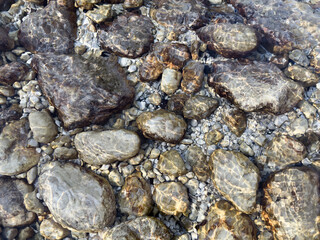 riverbed with underwater dark rocks under crystal clear water with sunlight and rippling pattern. shimmering organic texture. natural abstract background