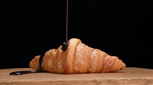 Delicious traditional croissant with a crispy golden texture. The croissant spins around itself and chocolate is slowly poured into it. A video that will whet your appetite.
