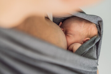 A loving mother breastfeeds her newborn baby while carrying them in a sling. A tender moment of...