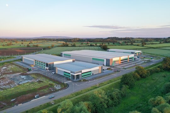 Aerial View of Modern Industrial Warehouse Complex in Green Countryside at Sunset – Commercial Buildings in Rural Setting