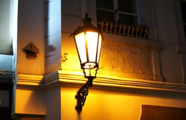 Classic black street lamp glowing warmly on the side of a building at night, illuminating...