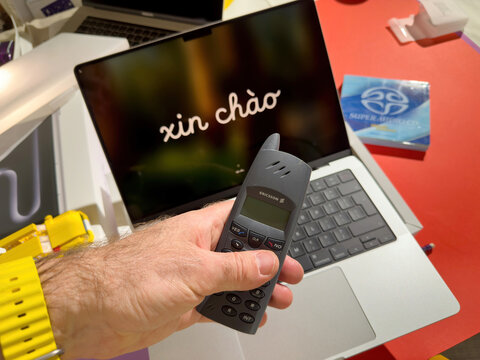 Paris, France - Mar 26, 2025: A hand wearing a yellow watch holds a vintage Ericsson DECT phone above an open MacBook Pro M4 Max with a welcome message xin cha o displayed on the screen