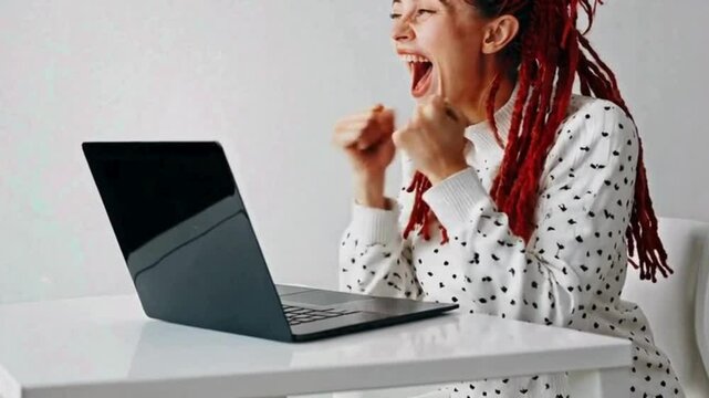 Excited woman with red dreadlocks celebrating at laptop

