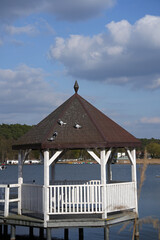 Several pigeons on the roof of a white gazebo by the lake.