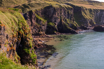 A rocky shoreline with a green cliff and a body of water