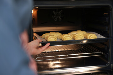 Woman putting baking sheet with raw croissants into oven, closeup