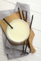 Delicious vanilla milk in glass and pods on white wooden table, top view