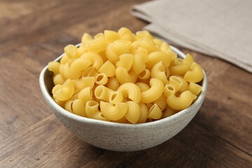 Raw horns pasta in bowl on wooden table, closeup
