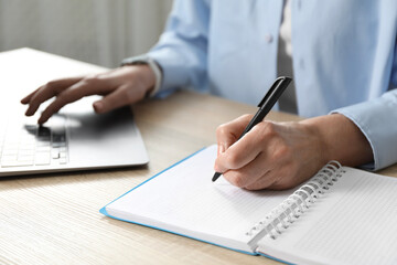 Woman learning online using laptop and taking notes at wooden table indoors, closeup. Self-study
