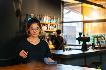 Small business entrepreneur coffee shop owner concept. Happy Asian woman cafe waitress employee using kitchen towel and cleanser cleaning table and preparing coffee shop to get ready for opening.