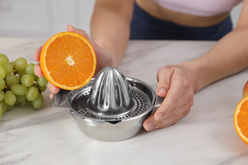 Woman with orange and juicer making juice at white marble table indoors, closeup