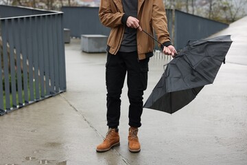 Man with broken umbrella fighting wind under rain outdoors, closeup
