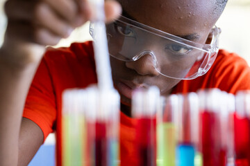 Conducting science experiment, student in school wearing safety goggles focusing on test tubes
