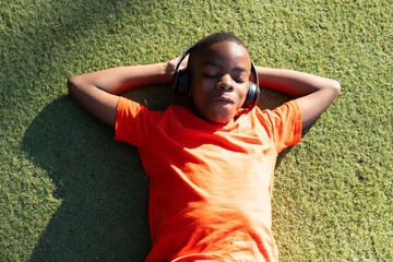 Listening to music, boy in orange shirt relaxing on grass outdoors